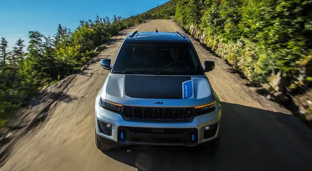 A silver and black 2023 Jeep Grand Cherokee 4xe is shown driving on a dirt road.