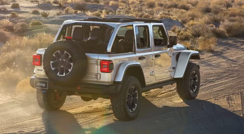 A silver 2024 Jeep Wrangler Rubicon is shown driving off-road.