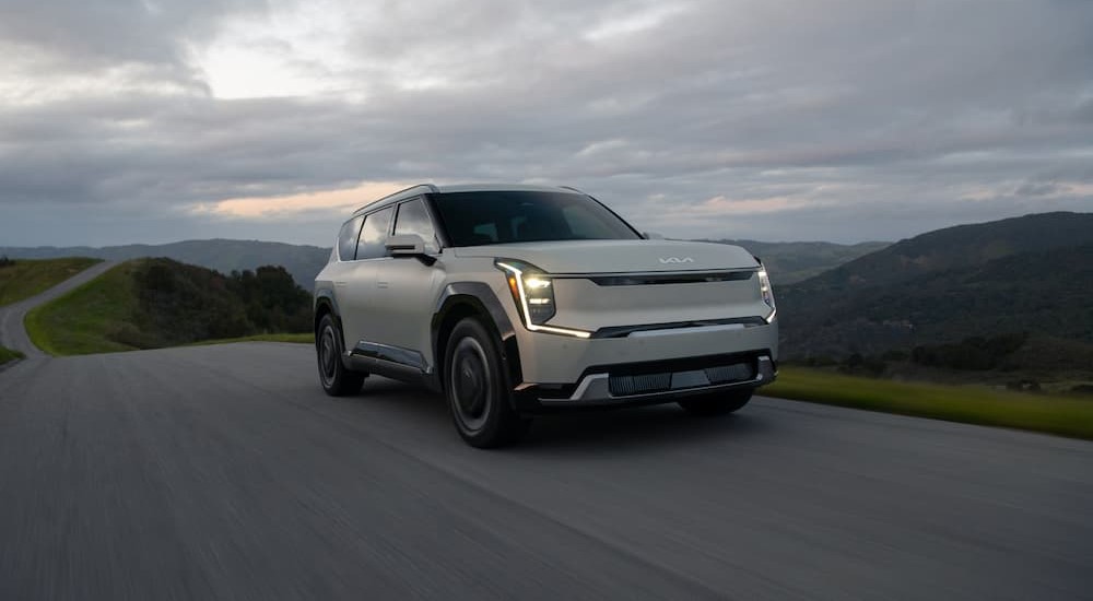 A white 2024 Kia EV9 is shown driving on a road.