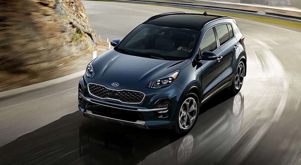 A blue 2020 Kia Sportage is shown driving on a highway.