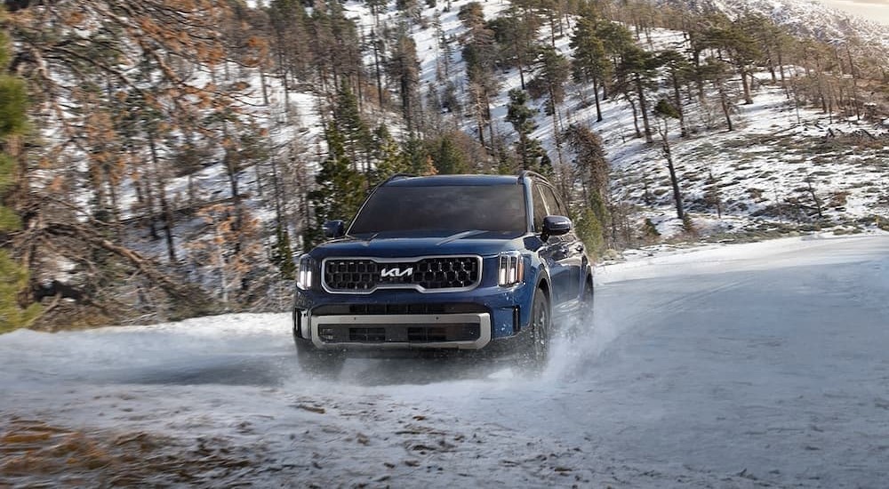 A blue 2023 Kia Telluride is shown driving on snow.