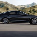 A black 2021 Kia K5 is shown driving on a road after visiting one of the most popular Kia dealerships in the area.