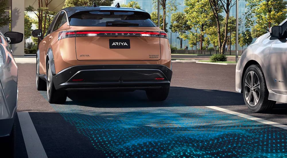 A copper 2022 Nissan Ariya is shown reversing into a parking spot.