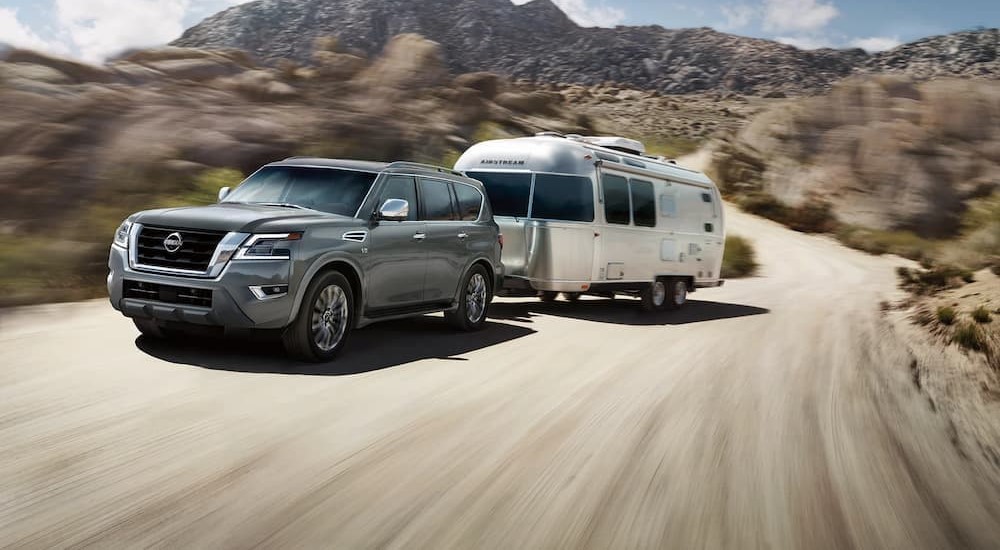 A gray 2023 Nissan Armada is shown towing a trailer on a dirt road.
