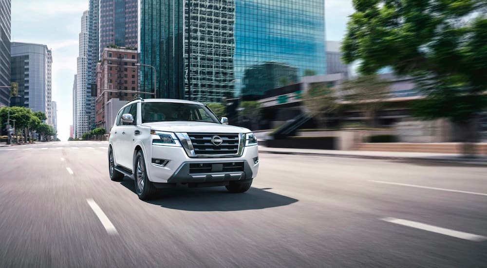 One of the most popular Nissan SUVs, a white 2023 Nissan Armada, is shown driving near city buildings.