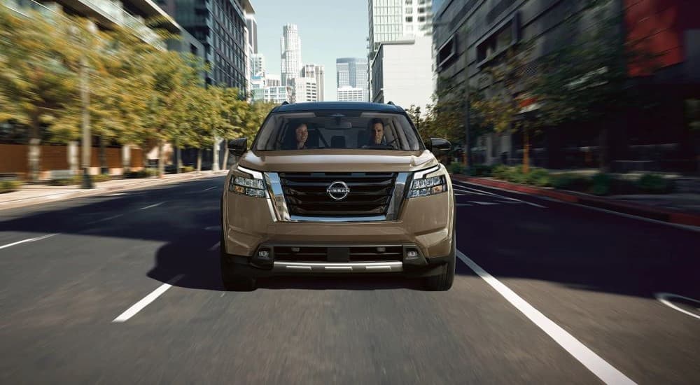 A tan 2023 Nissan Pathfinder is shown driving on a city road.