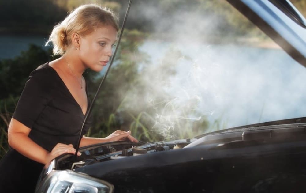 A woman is shown checking an overheated engine.