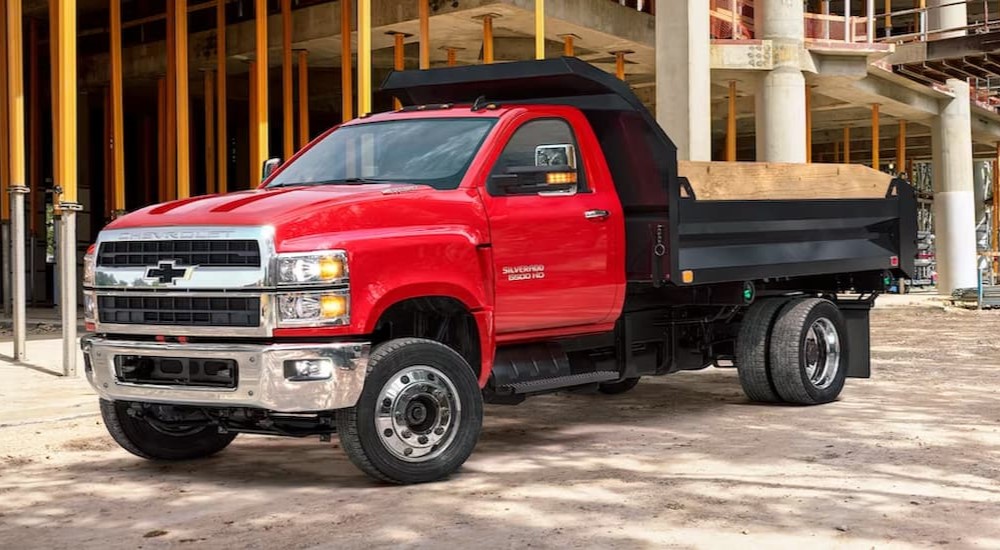 A red 2020 Chevy Silverado 6500HD is shown parked near a construction site after visiting a commercial truck dealer.