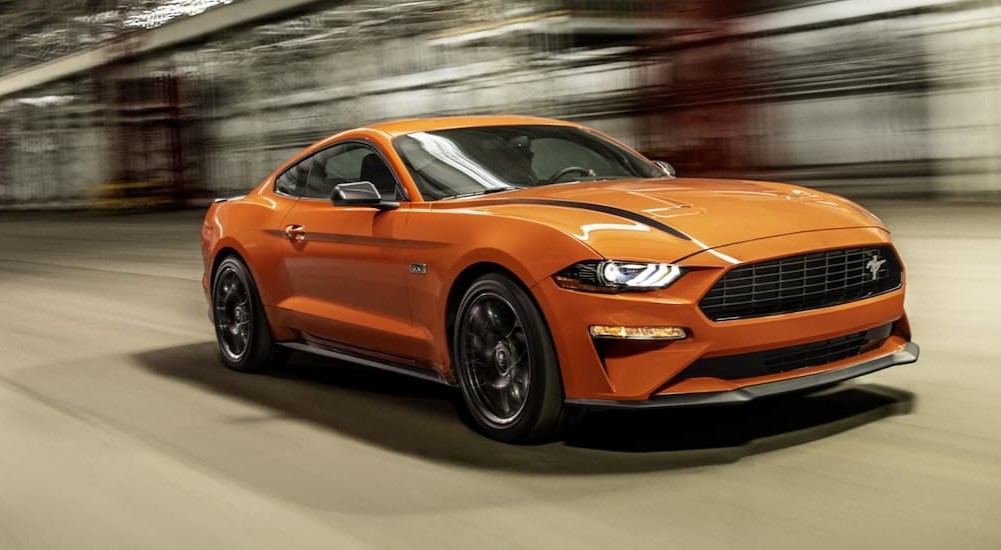 An orange 2021 Ford Mustang is shown driving on a road.