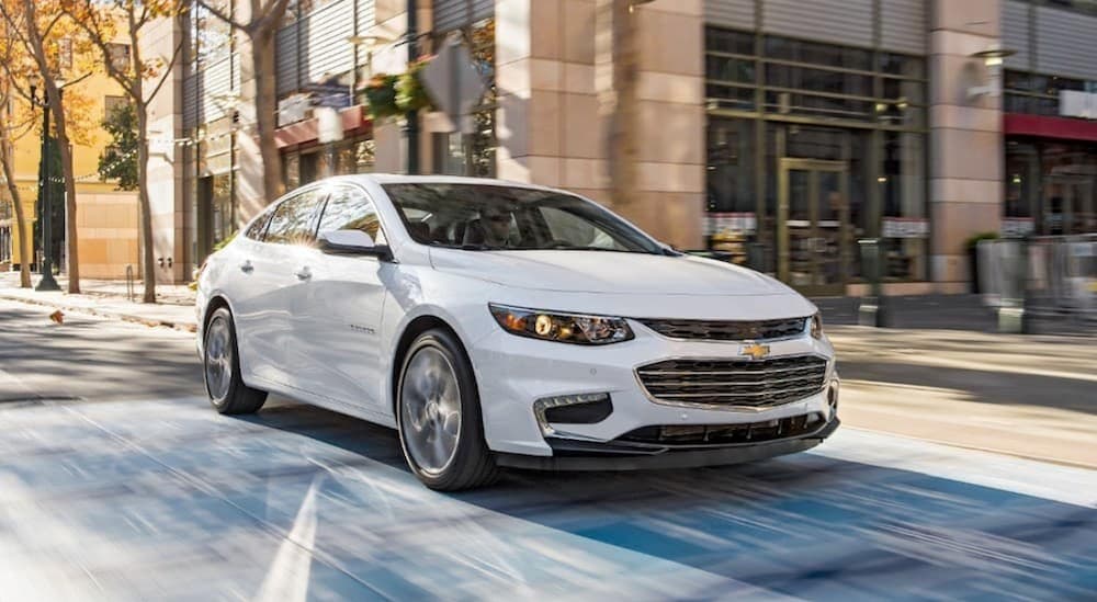 A white 22016 Chevy Malibu is shown driving on a city road.