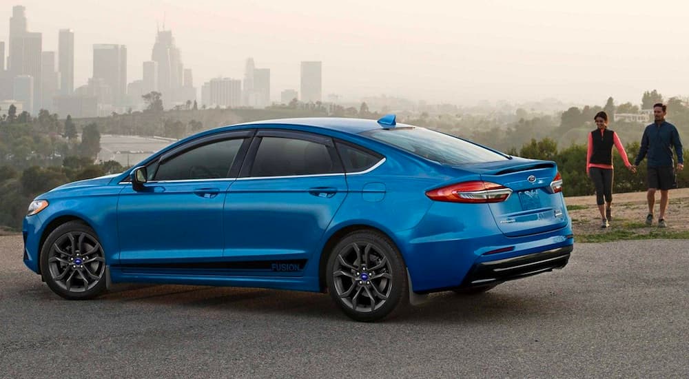 A blue 2020 Ford Fusion is shown parked near a city.