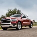 A red 2020 Ram 1500 is shown driving on a road from a used truck dealer.
