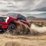 A red 2023 Ford F-150 Lightning is shown off-roading in a 2023 Ford F-150 vs 2023 GMC Sierra 1500 competition.