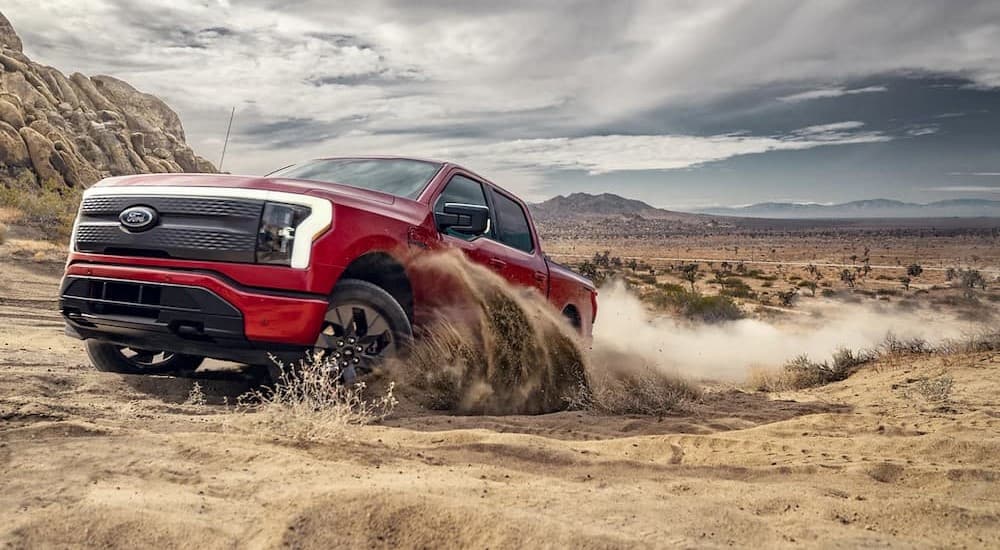A red 2023 Ford F-150 Lightning is shown off-roading in a 2023 Ford F-150 vs 2023 GMC Sierra 1500 competition.