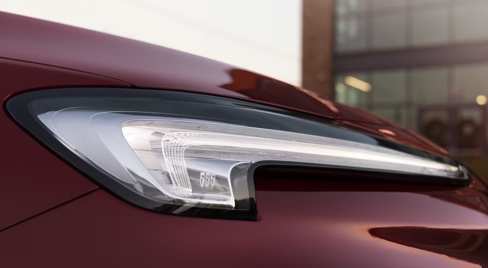 A close up shows the passenger side headlight on a maroon 2024 Buick Encore GX ST.
