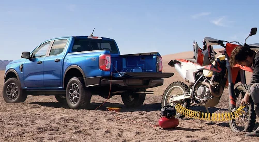 A blue 2024 Ford Ranger Sport 4X4 is shown parked off-road near a dirt bike.