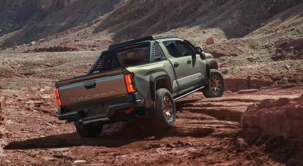 A green 2024 Toyota Tacoma Trailhunter is shown crawling over rocks.