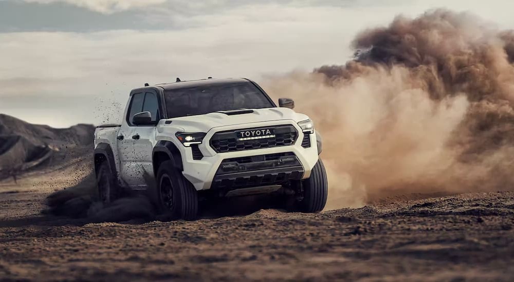 A white 2024 Toyota Tacoma is shown driving on the dirt.