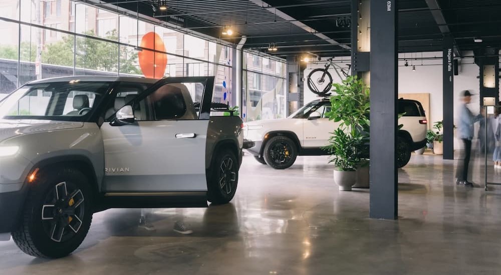 A silver 2023 Rivian R1T and a white 2023 Rivian R1S are shown parked in a showroom.