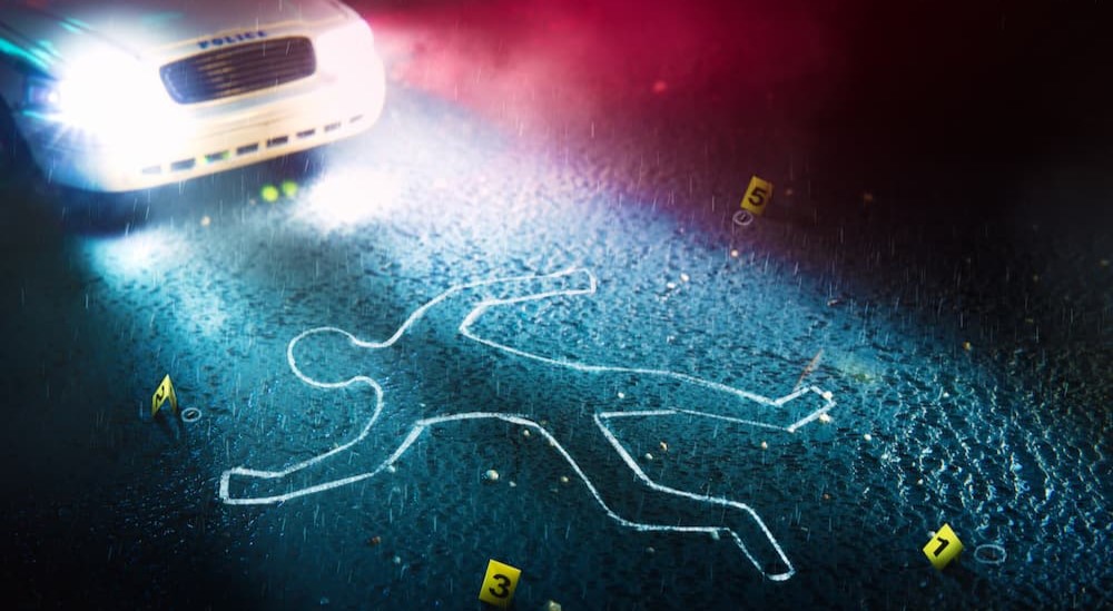 A police car is shown shining lights on a chalk outline.