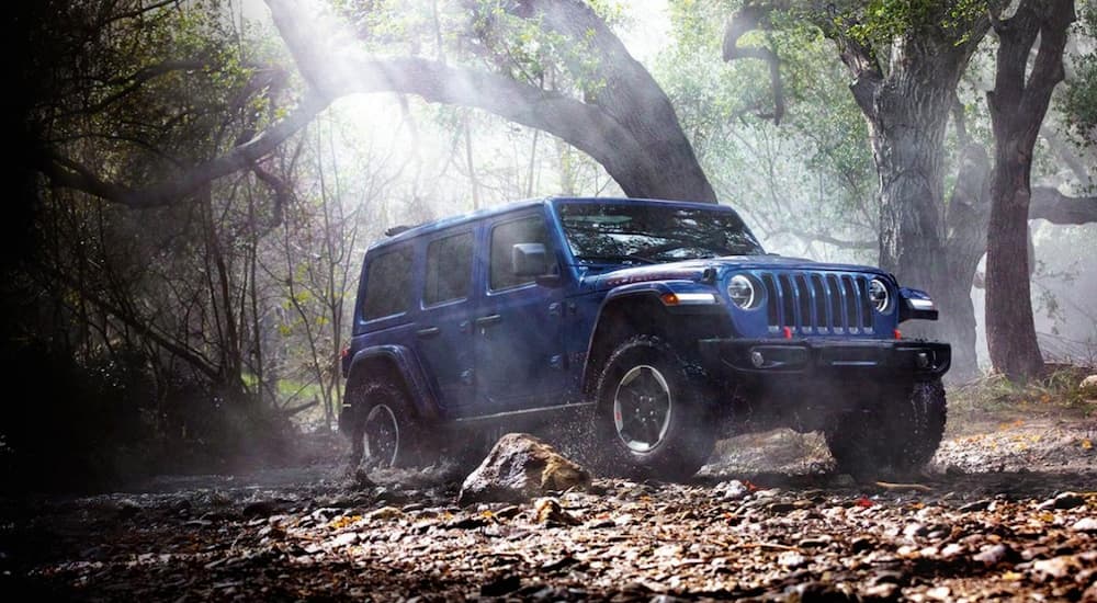 A popular vehicle for Jacksonville car sales, a blue 2020 Jeep Wrangler, is shown driving off-road.