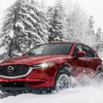 A red 2021 Mazda CX-5 for sale is show kicking up snow.