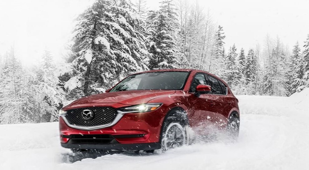 A red 2021 Mazda CX-5 for sale is show kicking up snow.