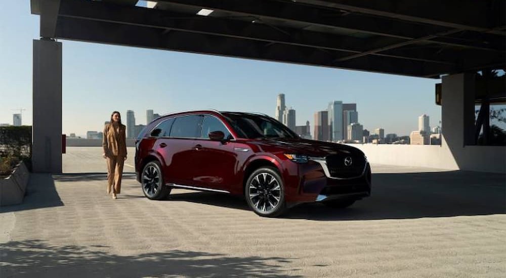 A red 2024 Mazda CX-90 is shown parked near a city after visiting a Mazda dealer.