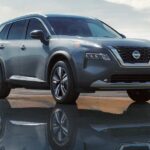 A silver 2023 Nissan Rogue is shown parked near a city.