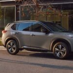 A grey 2023 Nissan Rogue is shown parked on the side of a city street.