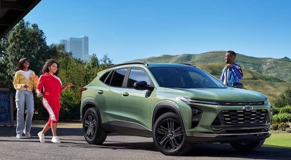 A green 2023 Chevy Trax is shown parked near several people near a city.