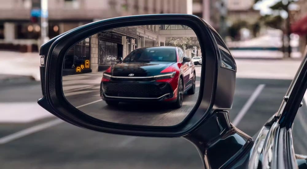 A red and black 2023 Toyota Crown is shown in a reflection of a sideview mirror.