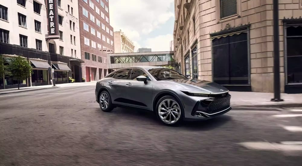 A silver 2023 Toyota Crown is shown driving around a corner on a city street.