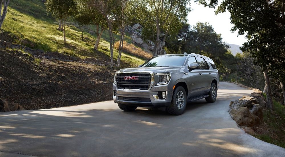 A grey 2021 GMC Yukon is shown driving on a tree-lined road.