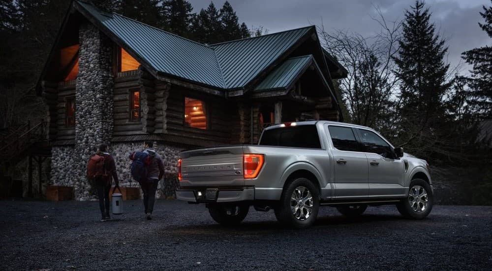 A popular used Ford F-150 for sale, a silver 2023 Ford F-150 Platinum, is shown parked near a log cabin.