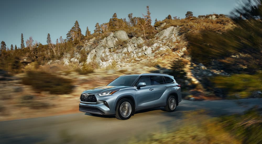 One of the most popular used SUVs for sale, a silver 2020 Toyota Highlander, is shown driving on a road.