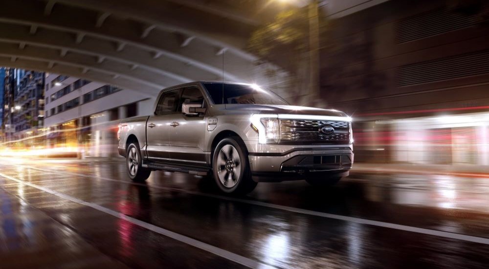 A silver 2023 Ford F-150 Lightning is shown driving on a wet city road.