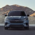 A grey 2023 Ford Mustang Mach-E is shown parked near a lake and mountains.