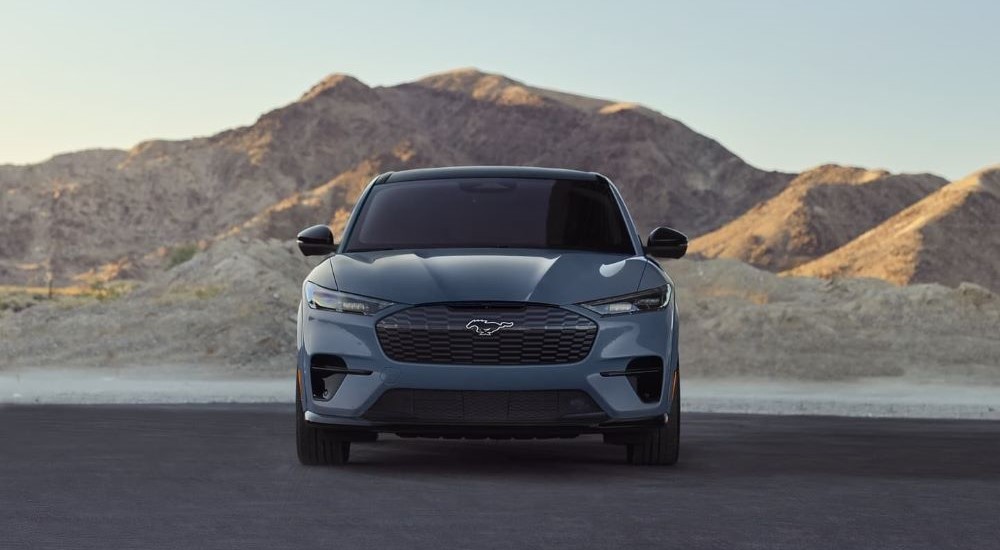 A grey 2023 Ford Mustang Mach-E is shown parked near a lake and mountains.