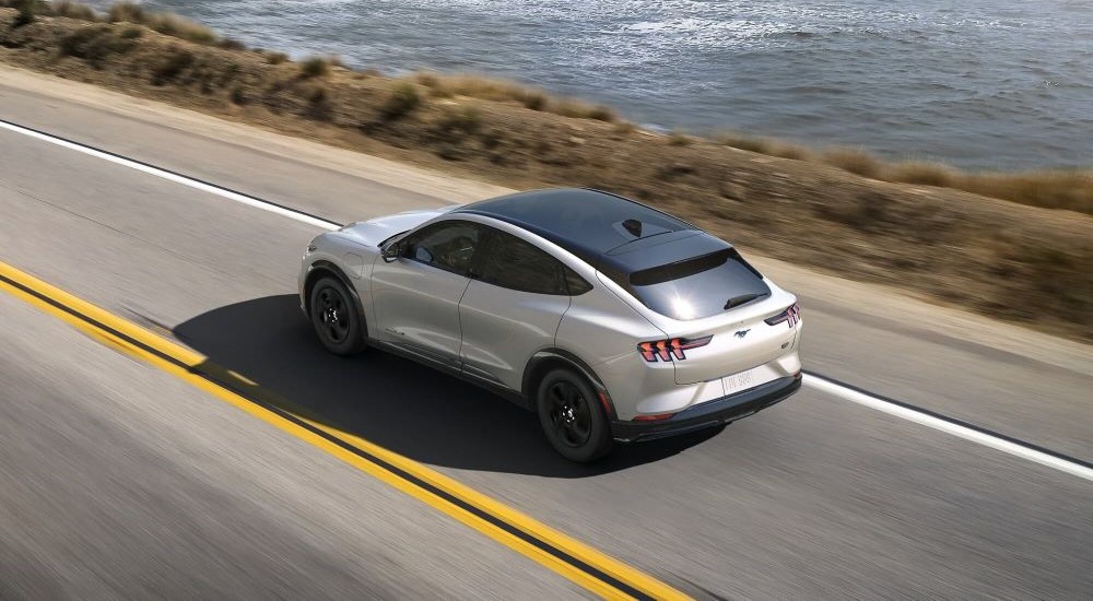 A white 2023 Ford Mustang Mach-E is shown driving near an ocean.