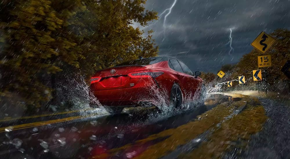 A red 2023 Toyota Camry is shown driving on a wet road near lightning.