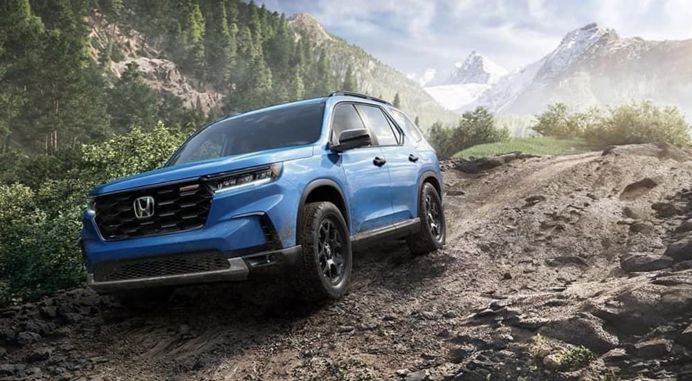 A blue 2023 Honda Pilot TrailSport is shown driving off-road.