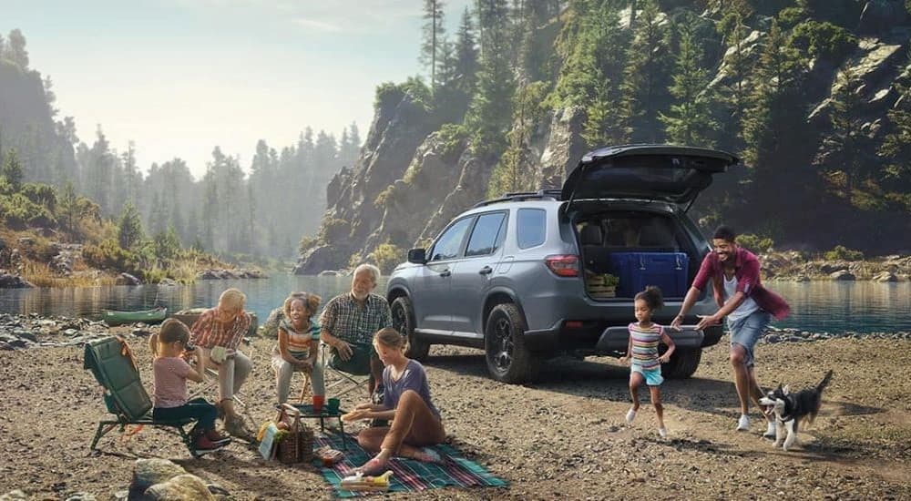 A gray 2023 Honda Pilot TrailSport is shown parked near a lake.