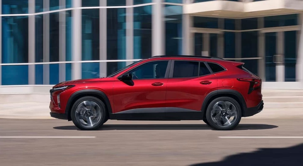 A red 2024 Chevy Trax is shown driving on a city street.