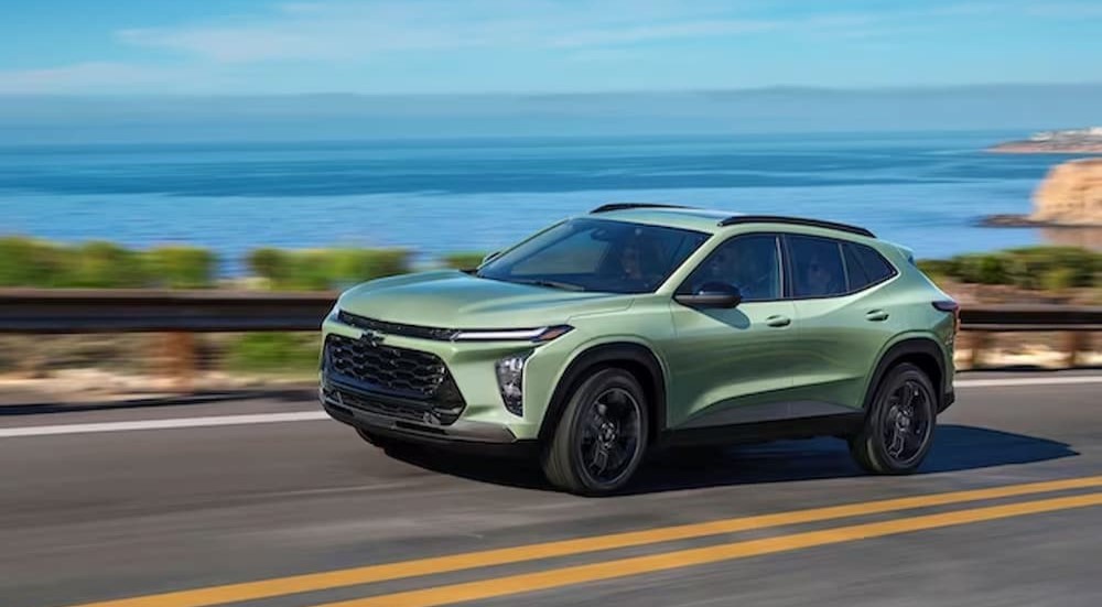 A green 2024 Chevy Trax is shown driving near an ocean.