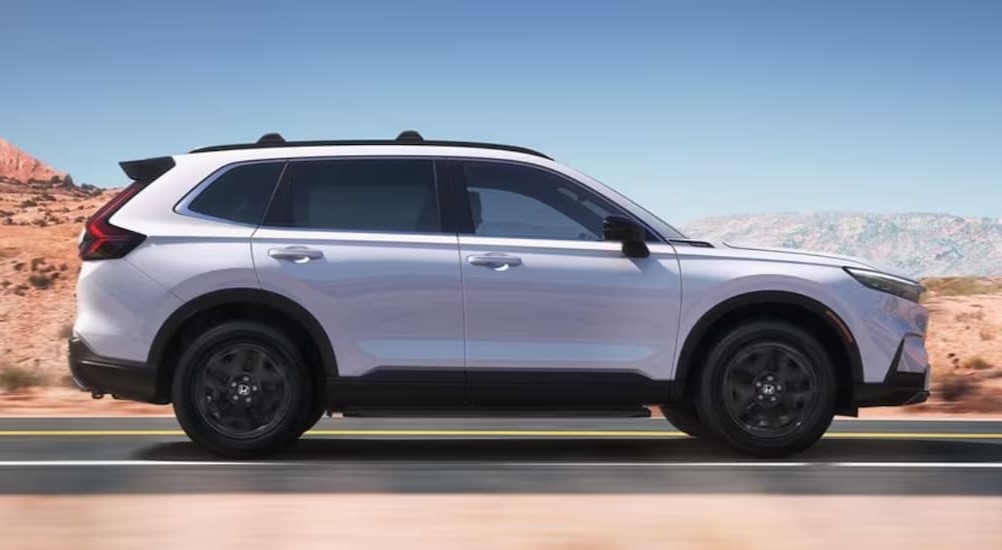 A white 2024 Honda CR-V sport Touring Hybrid is shown driving on a highway.