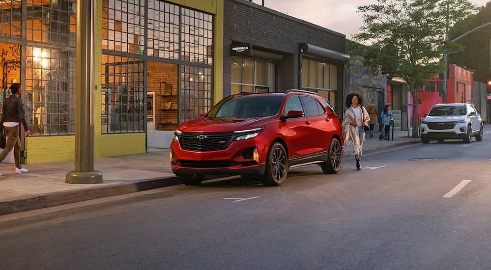A red 2024 Chevy Equinox RS is shown parked on a city street near a clothing shop.
