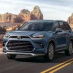 A blue 2024 Toyota Grand Highlander is shown driving on a highway.