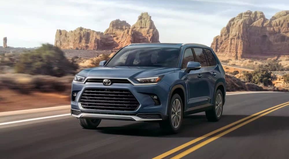 A blue 2024 Toyota Grand Highlander is shown driving on a highway.