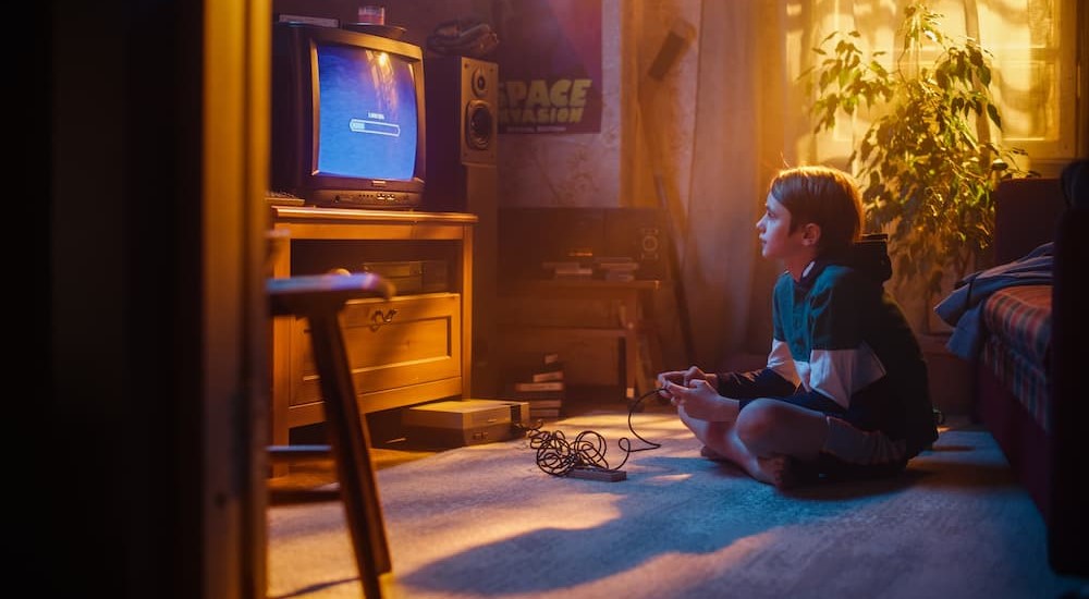 Cars in Games Part Two: A boy is shown playing a gaming console on a television.